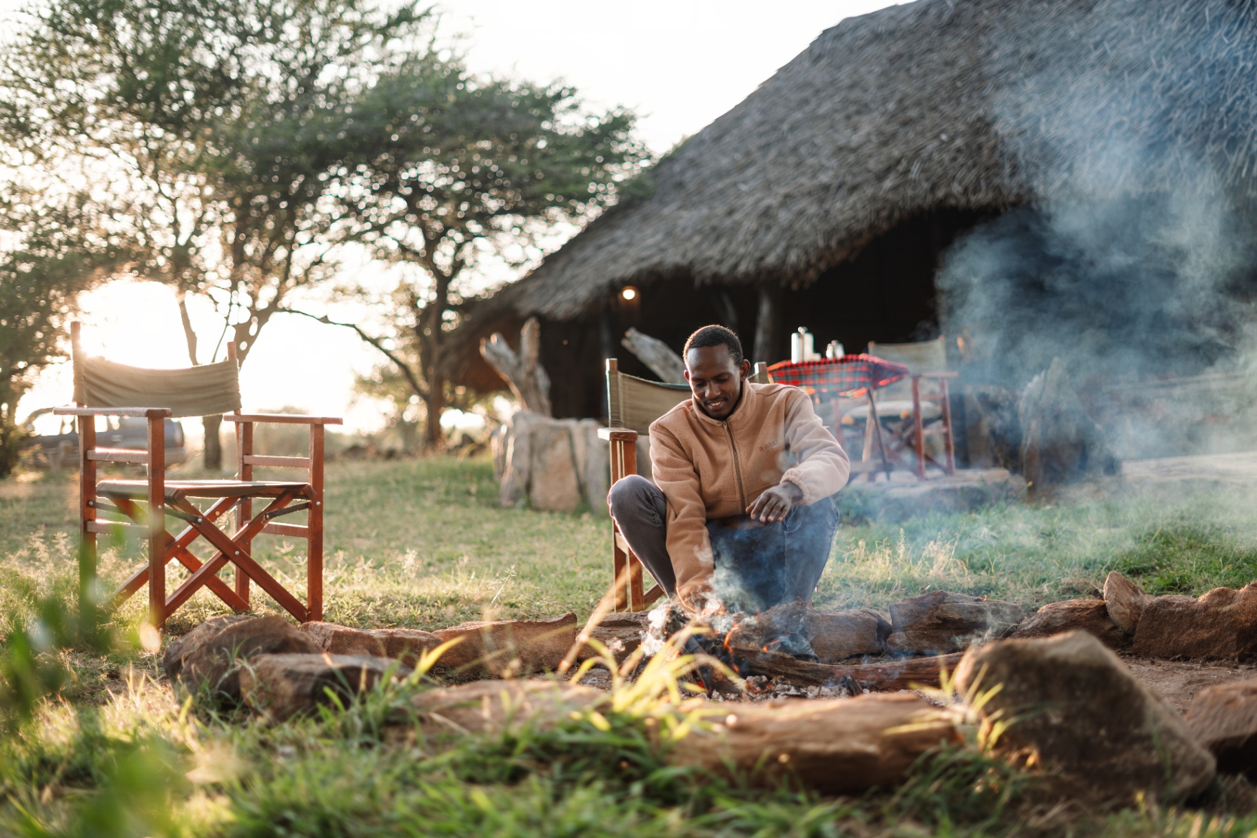 Camp attendant lighting the evening fire outside a thatched building